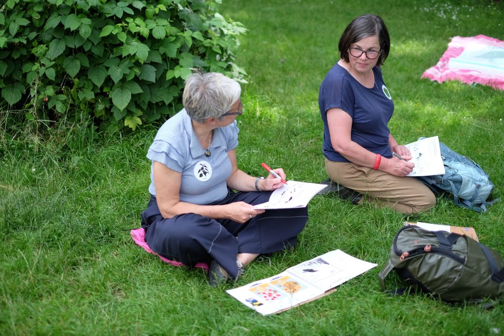 Two women sit in a garden and are working on their activity books
