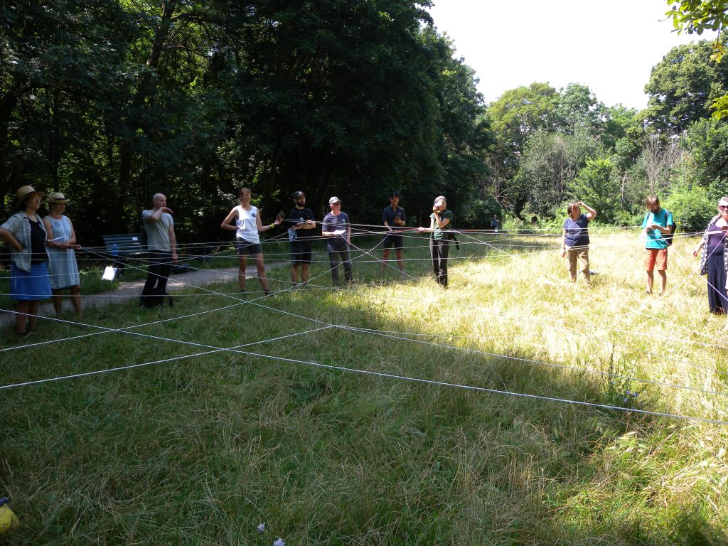 Group of people standing in a circle in a grassy field, with a web of string connecting between them
